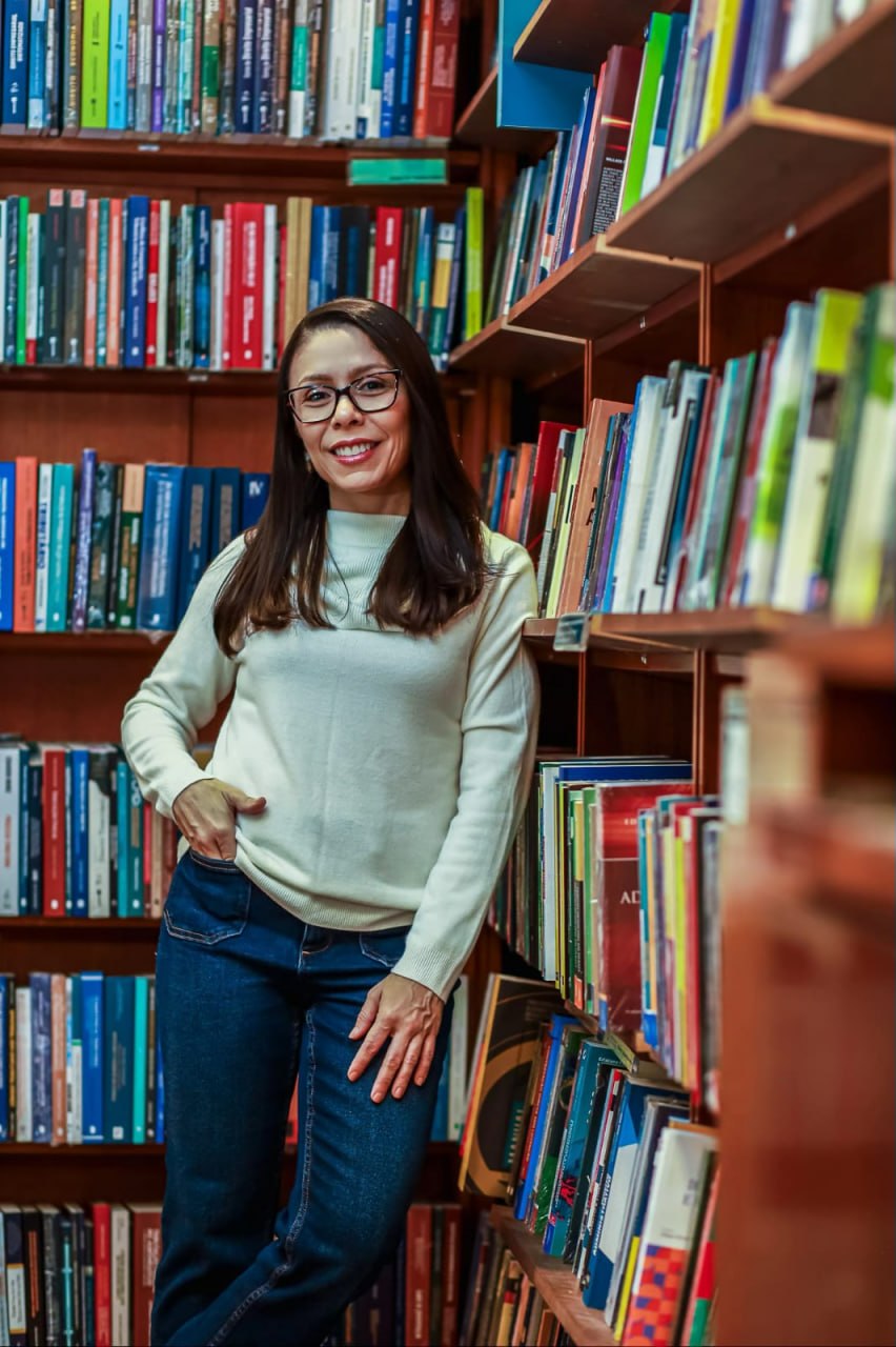 Silvia Morais entre estantes de livros em uma biblioteca